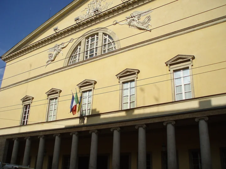 The upper facade of the Teatro Regio with a large lunette window, relief figures of winged Fame and two flags