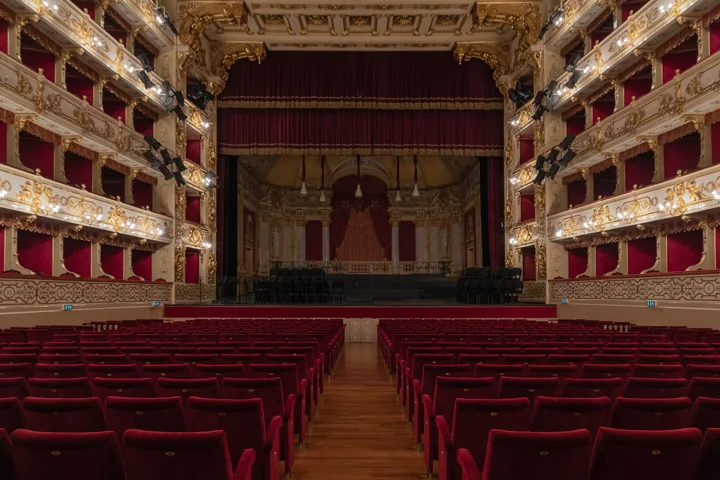 Red velvet stalls facing the stage of the Teatro Regio, between gilded tiers of red boxes