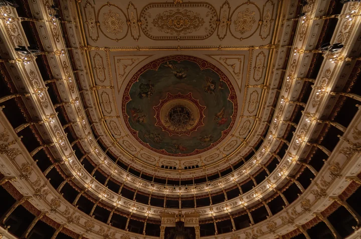 The upper tiers of the Teatro Regio seen from below, rising in lit gilded rings to a round painted ceiling